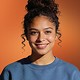 Smiling young woman with curly hair wearing a light blue top, portrait on orange background